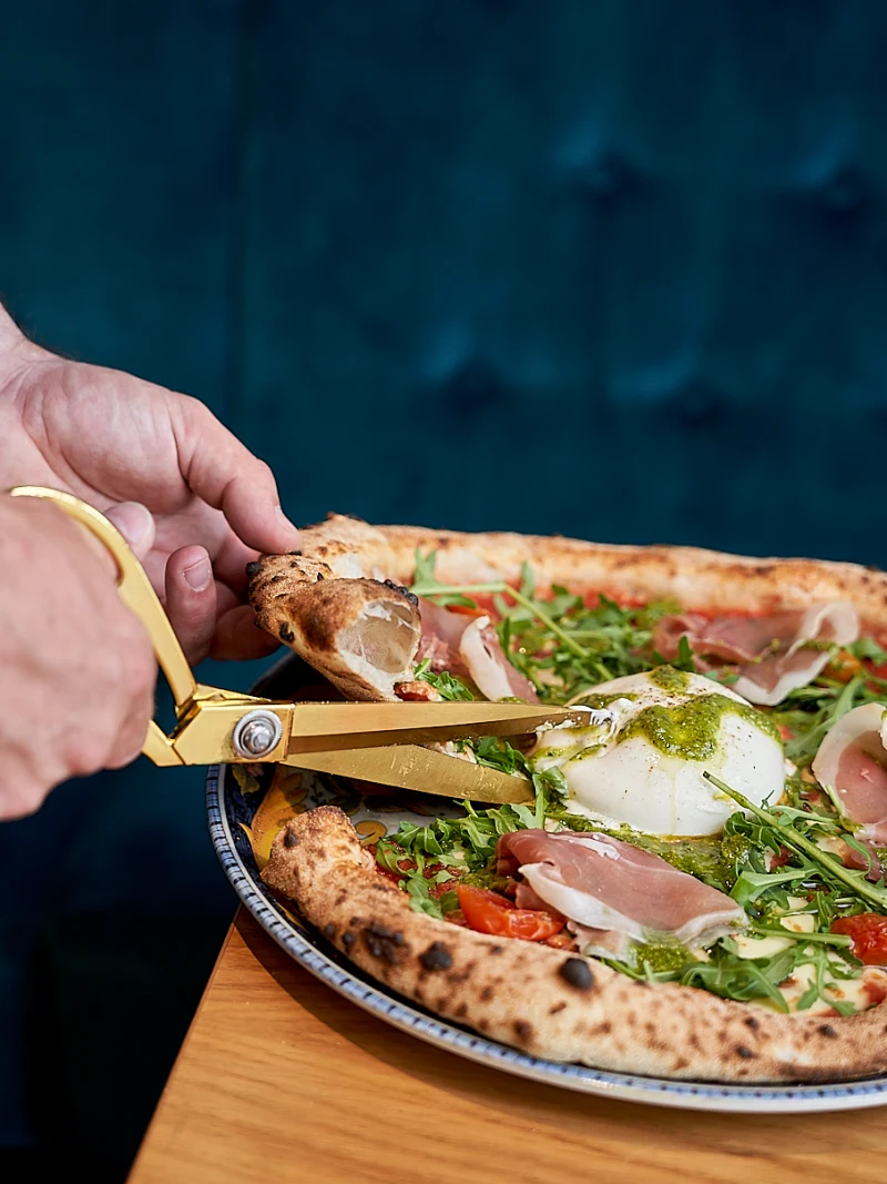 Pizza Napoletana wird frisch mit der Pizzaschere geschnitten